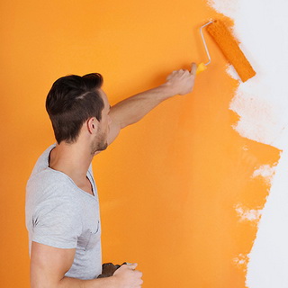 Красит стену оранжевой краской